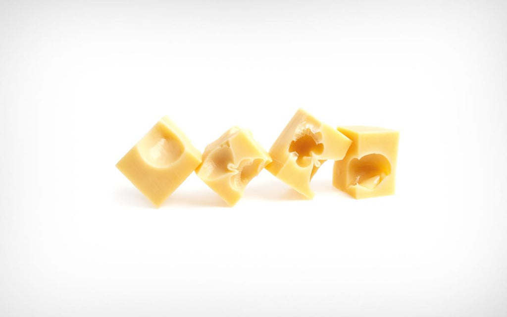 Four square pieces of Swiss-type cheese, showing internal holes (eyes), arranged on a white background.