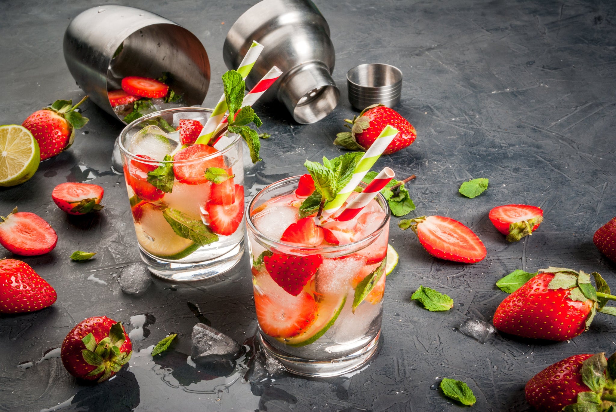 Strawberry and lime cocktails with mint and ice, surrounded by fresh fruit and a cocktail shaker.
