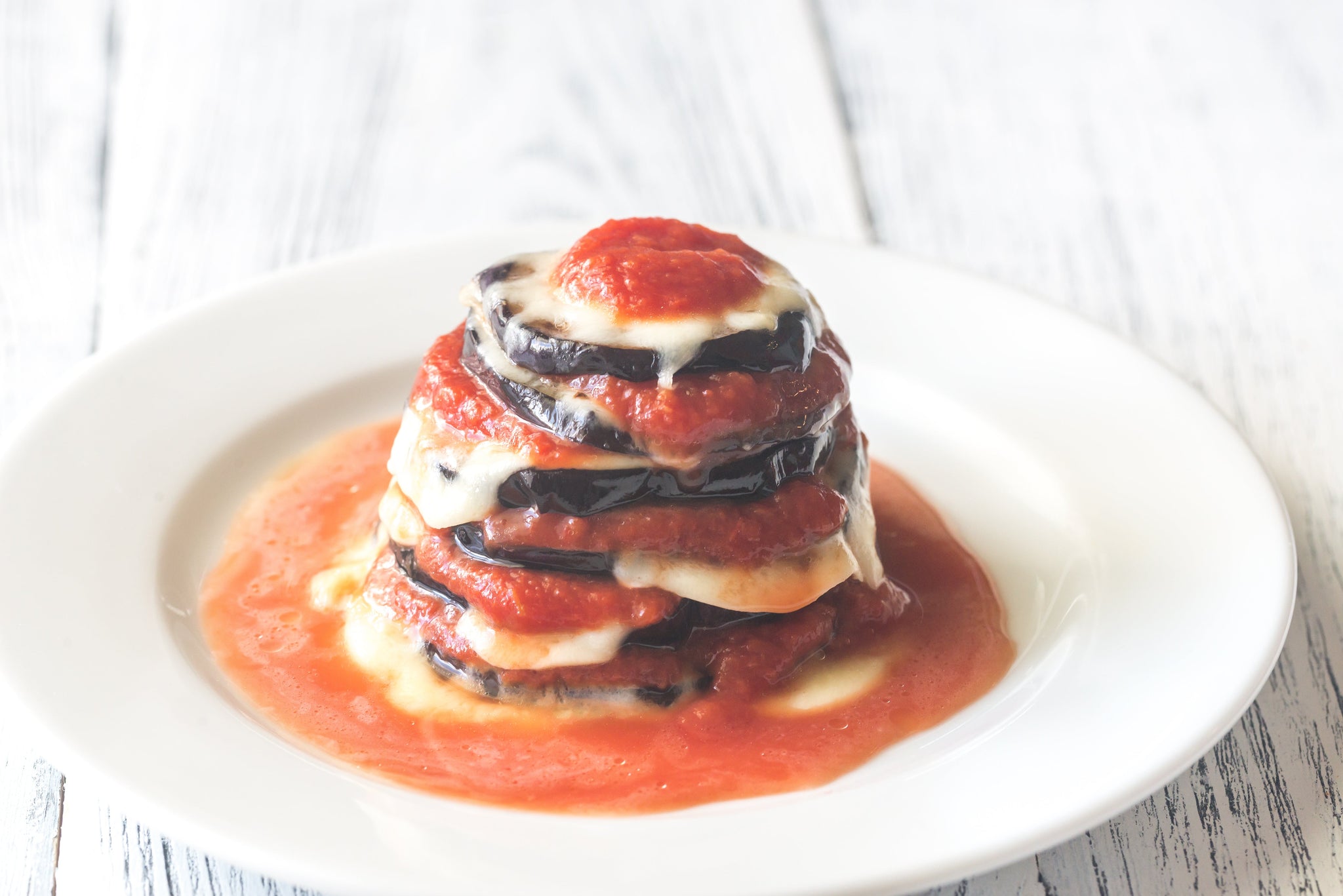 Stacked eggplant and melted cheese layered with tomato sauce, served on a white plate.