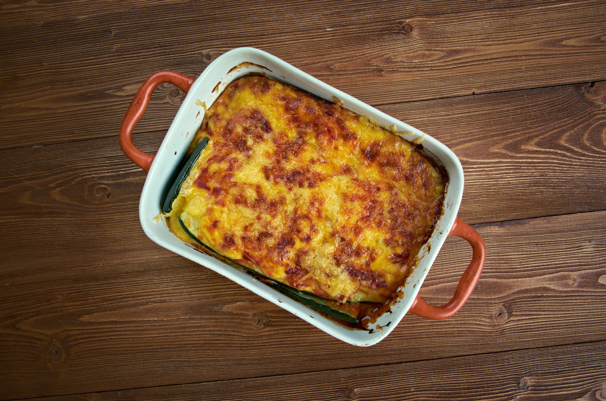 Baked zucchini lasagna in a white casserole dish with melted golden cheese on top.