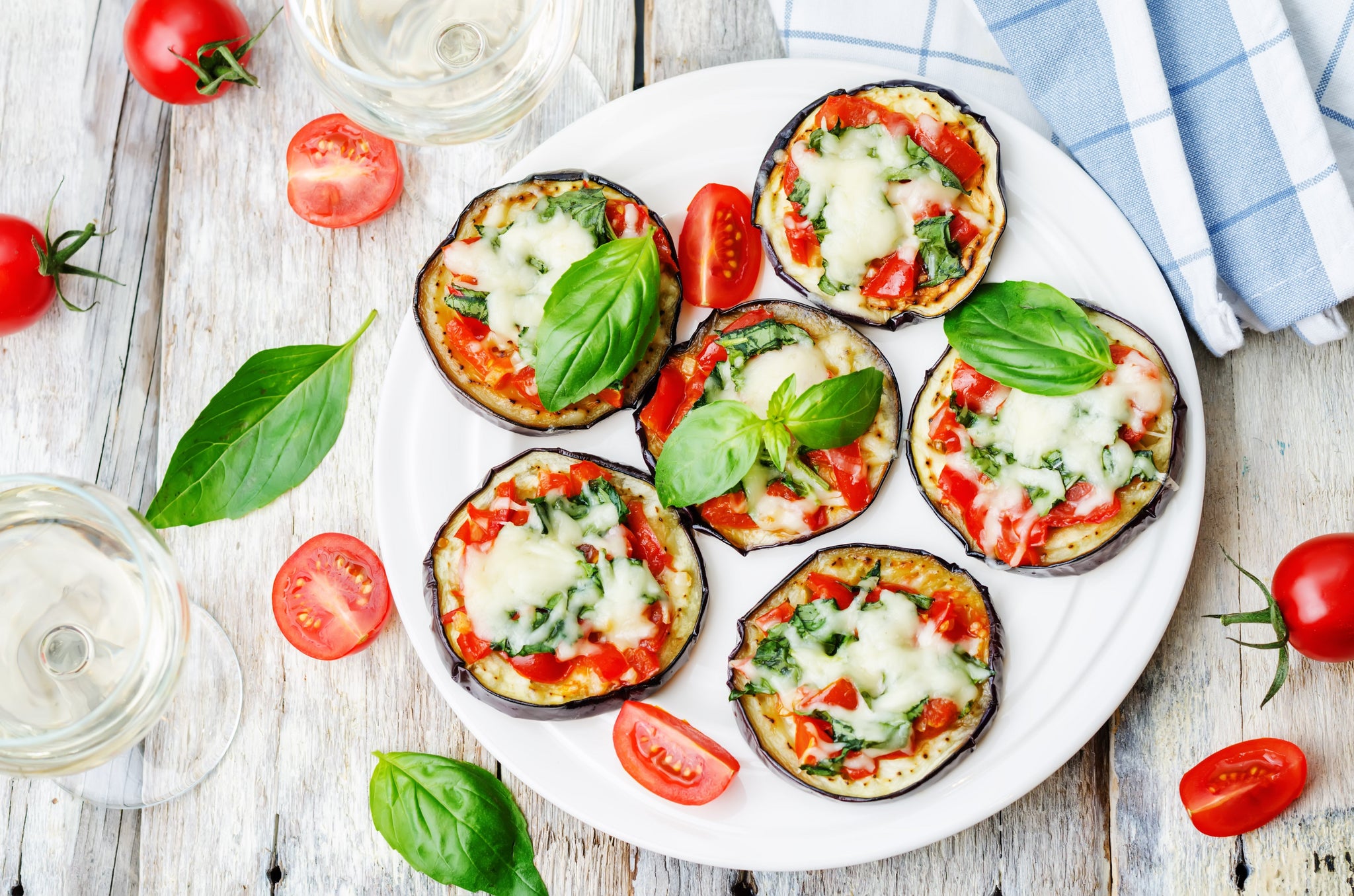 Mini eggplant pizzas topped with melted cheese, tomatoes, and basil on a white plate.