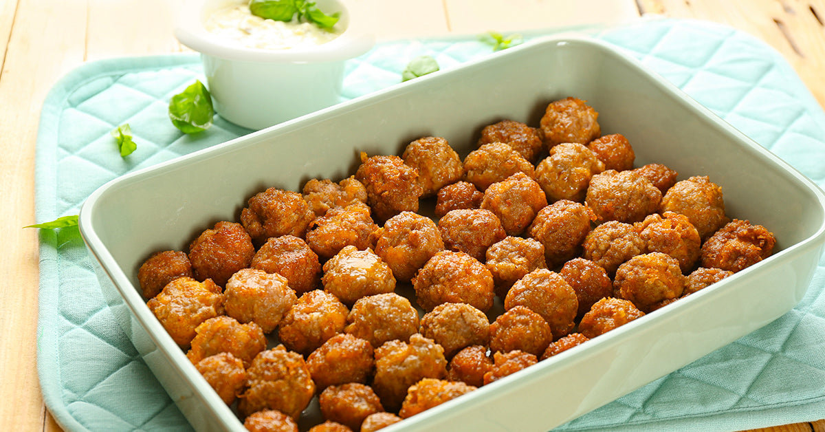Baking dish filled with golden-brown meatballs with a small bowl of dipping sauce in the background.