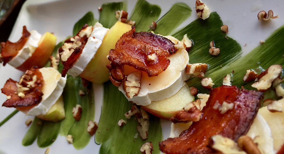 Apple slices topped with creamy cheese, crispy bacon, and chopped nuts, arranged decoratively on a green-painted plate.