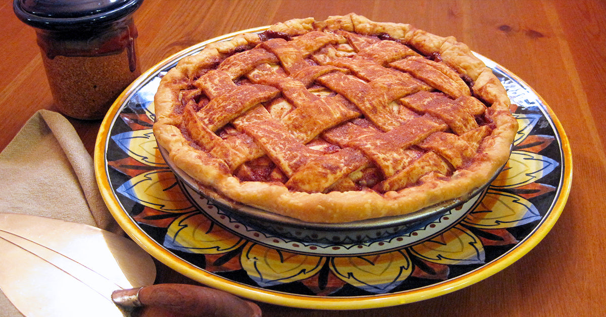 Lattice-topped pie on a decorative plate with a jar, napkin, and pie server beside it.