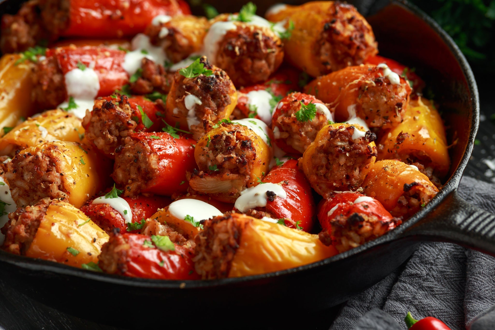 Skillet filled with baked stuffed mini peppers topped with herbs and a drizzle of creamy sauce.