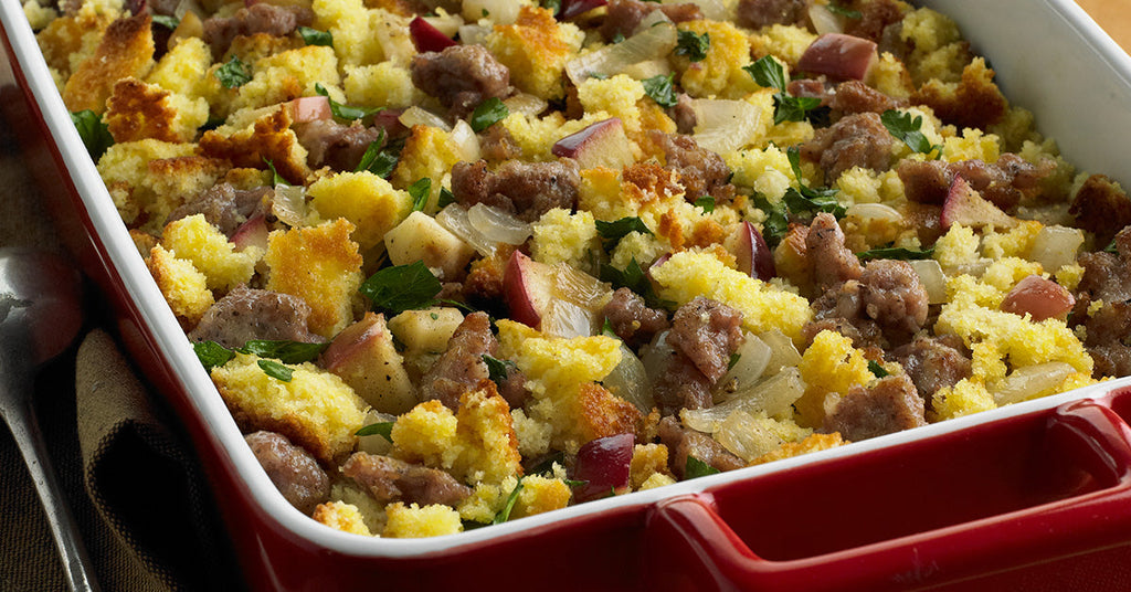 Baked cornbread stuffing with sausage, apples, onions, and herbs in a red casserole dish.
