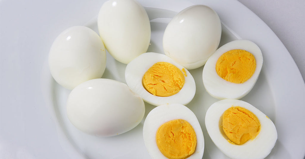 A white plate holds several boiled eggs, some whole and others cut in half to reveal their bright yellow yolks, arranged neatly for presentation.