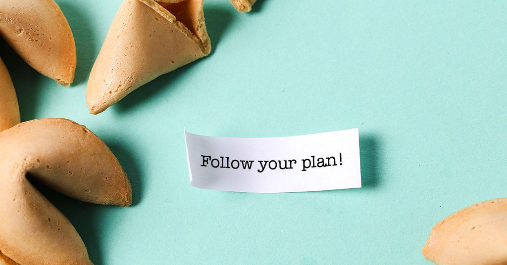 Fortune cookies with a message slip reading Follow your plan! on a mint-green background.