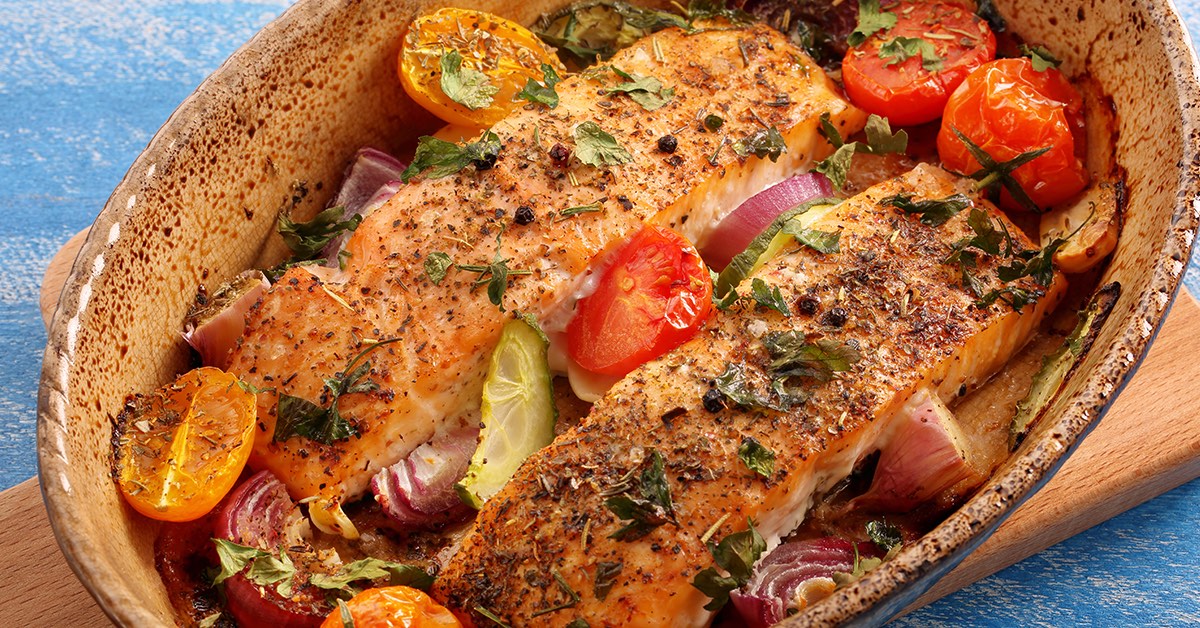 Seasoned baked salmon fillets in a dish with tomatoes, red onions, and herbs.