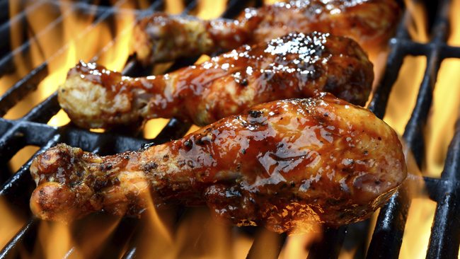 Glazed chicken drumsticks grilling over open flames.
