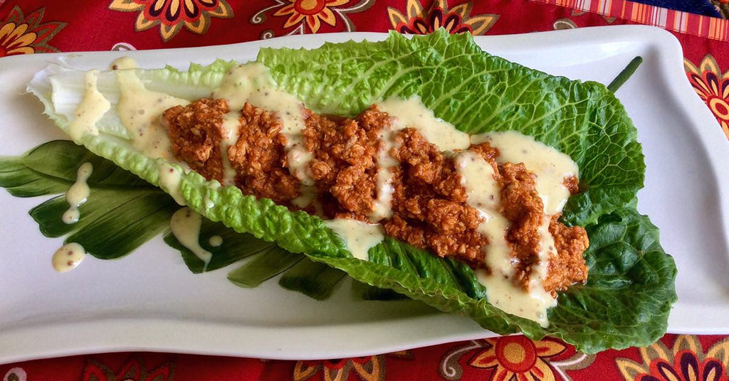 Romaine lettuce leaf filled with seasoned ground meat and drizzled with creamy dressing on a decorative plate.