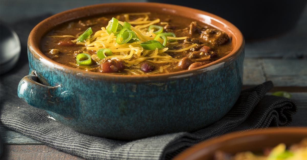 Hearty chili in a rustic bowl topped with shredded cheese and sliced green onions.