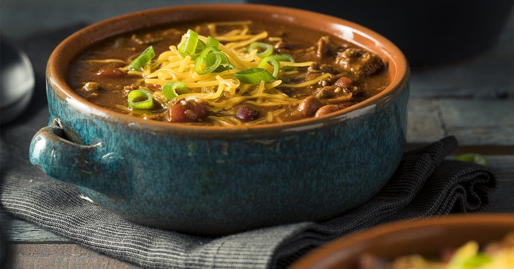 Bowl of hearty chili topped with shredded cheese and sliced green onions.