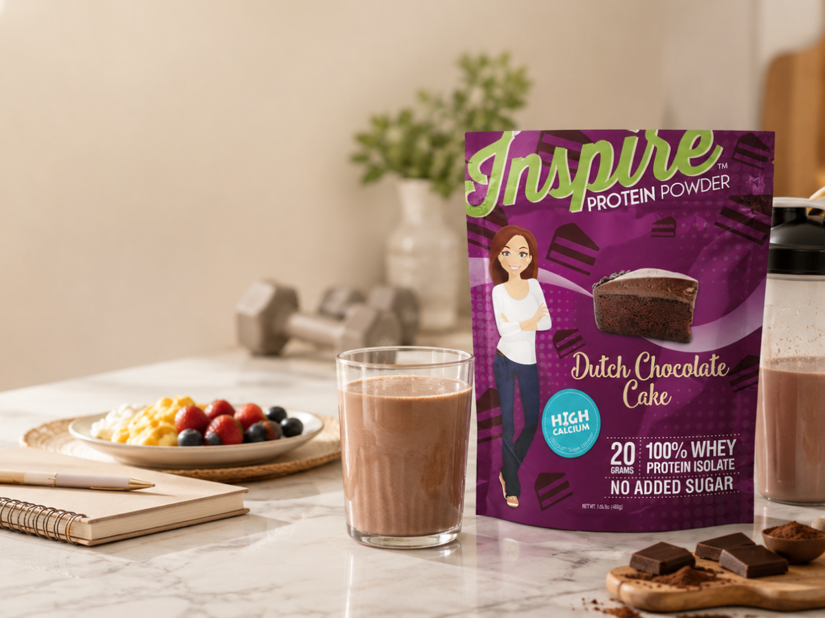 Inspire Dutch Chocolate Cake Protein Powder with a chocolate protein shake, shaker bottle, protein-focused breakfast, water, journal, and dumbbells in a bright kitchen.