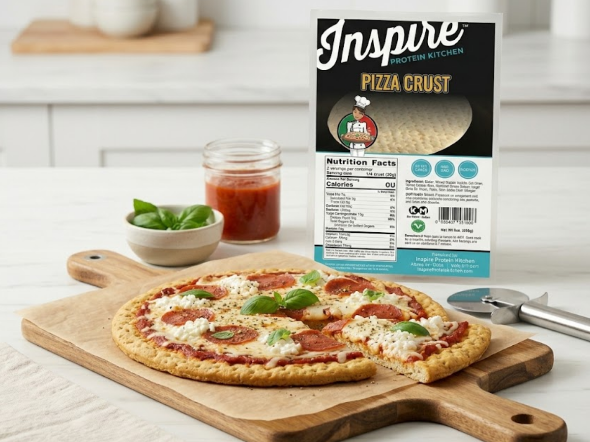 High-protein cottage cheese pizza made with Inspire Protein Kitchen Pizza Crust, topped with mozzarella and turkey pepperoni, with the Inspire Protein Kitchen Pizza Crust packaging displayed beside it in a bright kitchen setting.