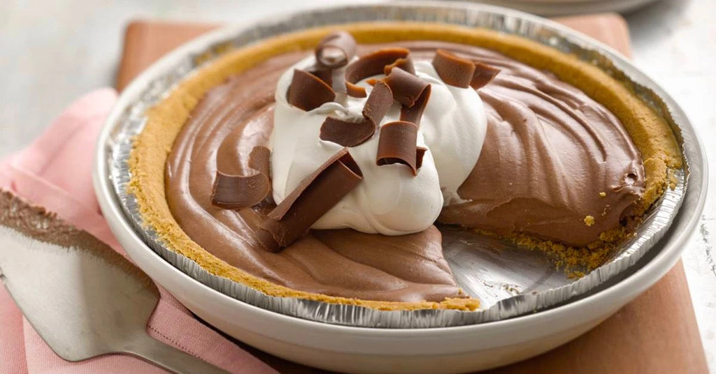 Chocolate cream pie with a slice removed, topped with whipped cream and chocolate curls in a graham crust.