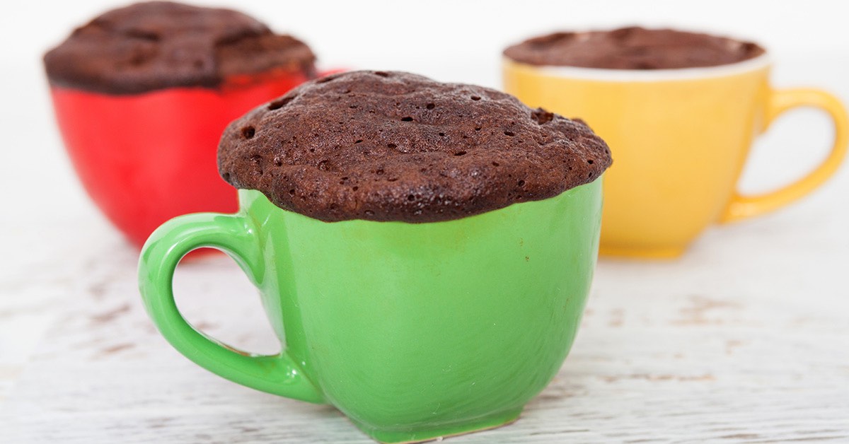 Chocolate mug cakes rising over the rims of colorful cups, with green, red, and yellow mugs on a light surface.