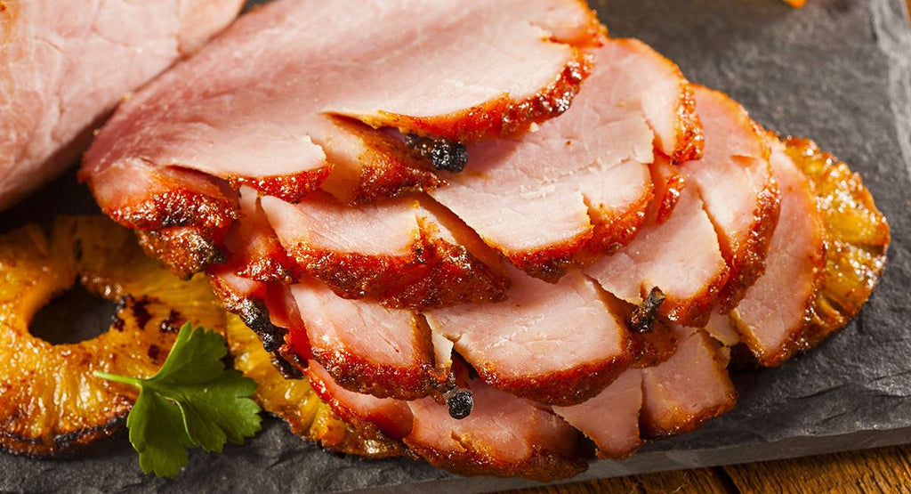 Slices of glazed roasted ham arranged on pineapple rings with a garnish of fresh parsley.
