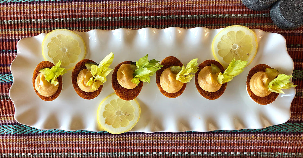 Plate of bite sized appetizers topped with creamy filling and celery, garnished with lemon slices.