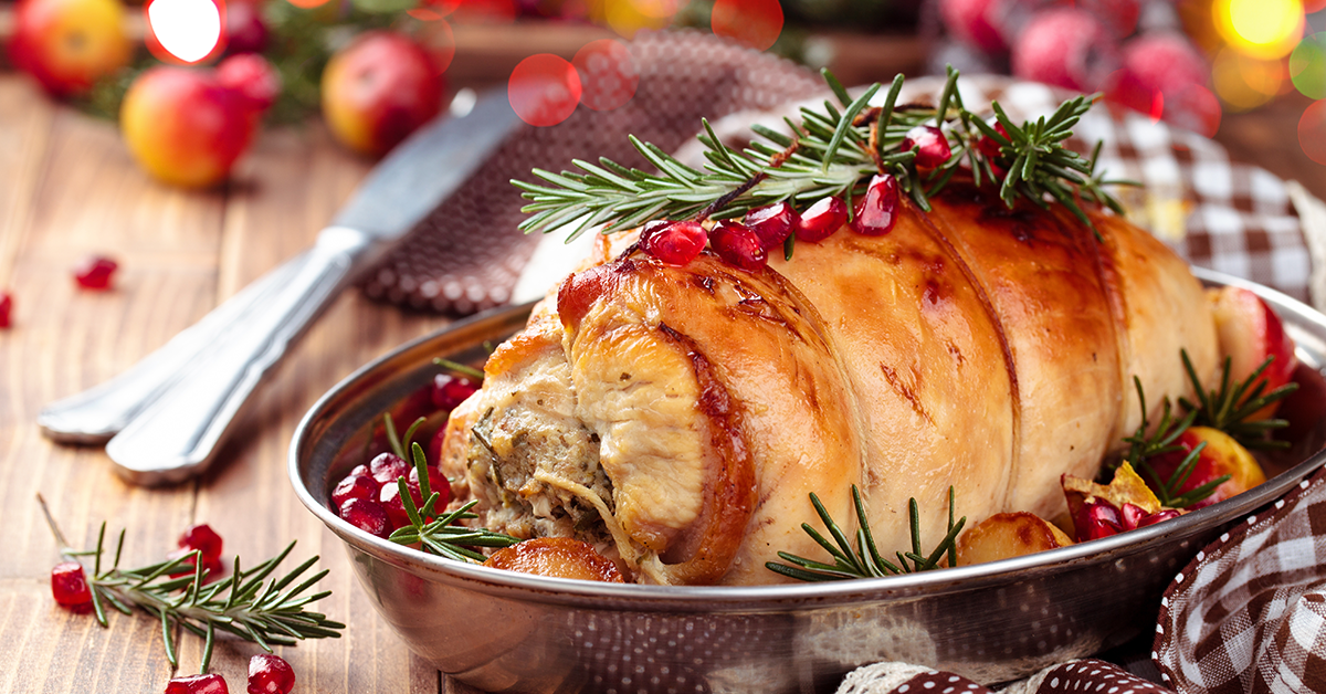 Roasted stuffed turkey roulade garnished with rosemary and pomegranate seeds in a serving dish.