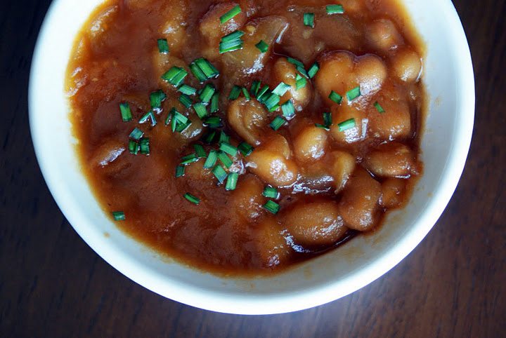 Bowl of baked beans in rich sauce topped with chopped chives.