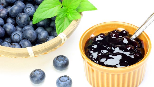 Fresh blueberries in a basket beside a small bowl of blueberry jam with a spoon.