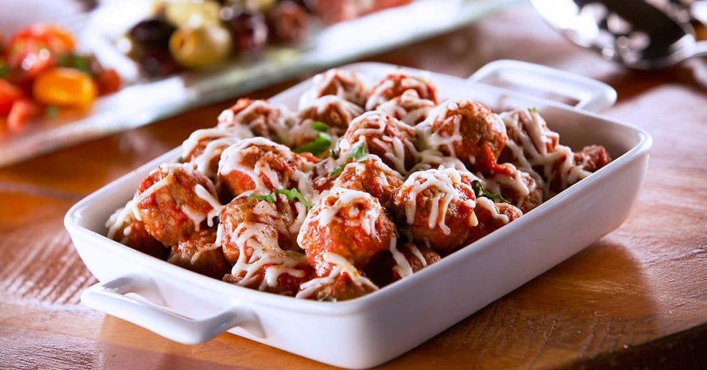 Baked meatballs in marinara sauce topped with melted cheese, served in a white rectangular dish.