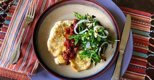 Plate with mashed potatoes, tomato-topped chicken, and a fresh arugula salad with onions and pine nuts.