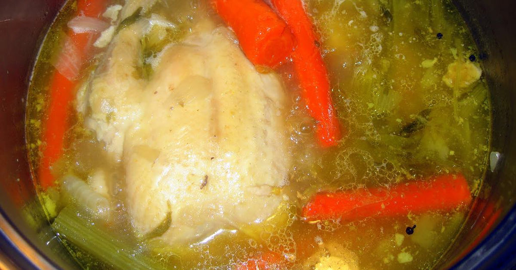 Whole chicken simmering in broth with carrots, celery, onions, and spices.