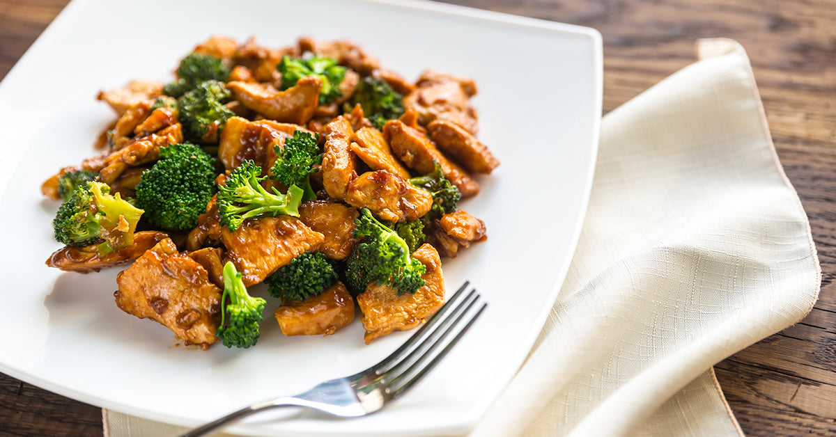 Stir-fried chicken and broccoli in a brown sauce served on a white plate with a fork.