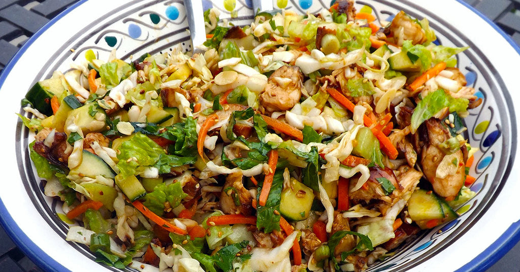 Colorful chopped salad with lettuce, carrots, cucumbers, and chicken in a patterned bowl.