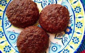 Three round, dark brown cookies are arranged on a colorful, decorative plate featuring blue and green floral patterns.