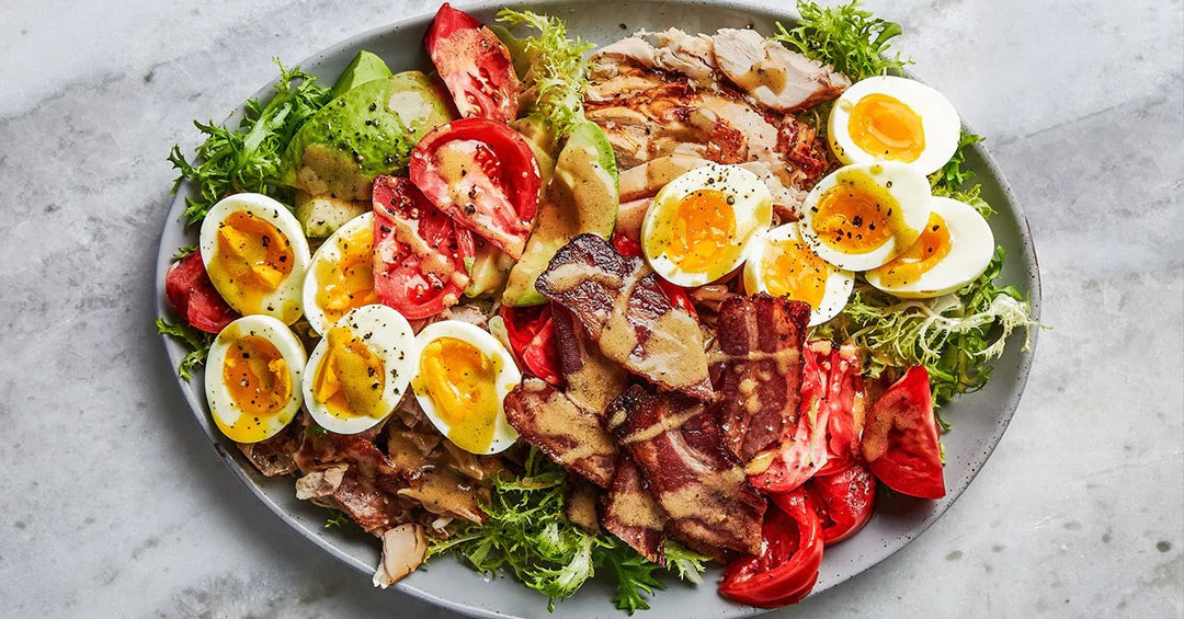 Colorful salad with soft-boiled eggs, tomatoes, avocado, bacon, greens, and sliced chicken drizzled with dressing.