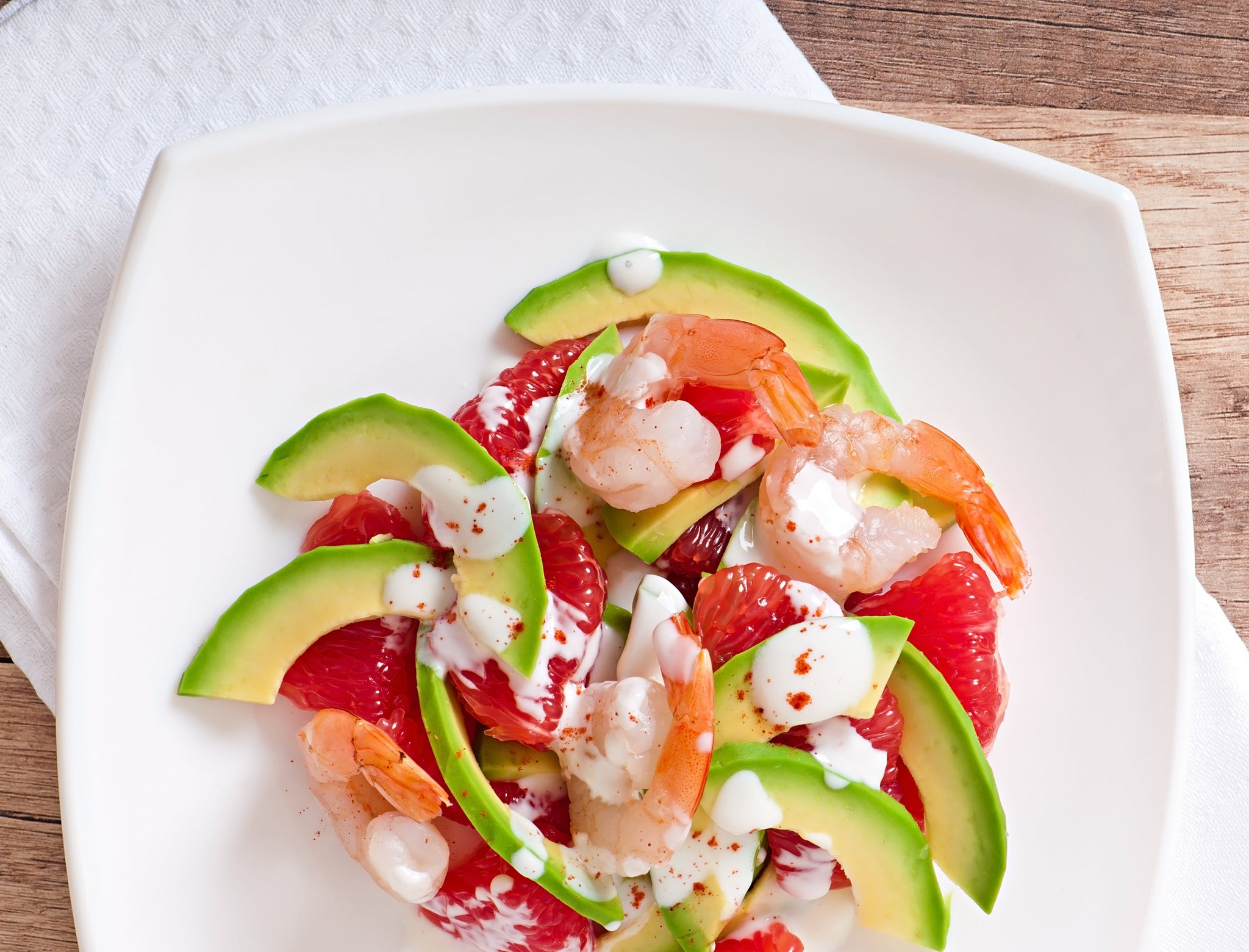 Shrimp salad with avocado slices, grapefruit segments, and creamy dressing on a white plate.