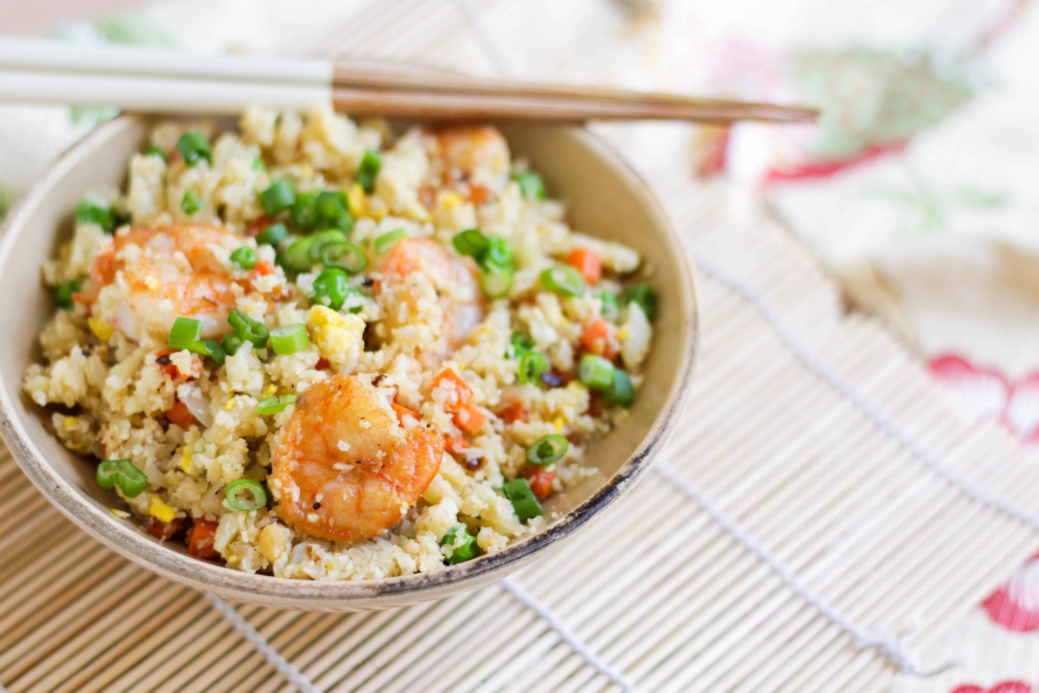 Bowl of shrimp fried rice with vegetables and green onions, with chopsticks resting on the rim.