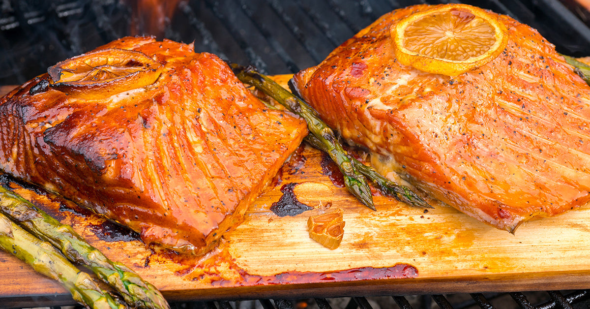 Glazed salmon fillets grilled on a wooden plank with lemon slices and asparagus.