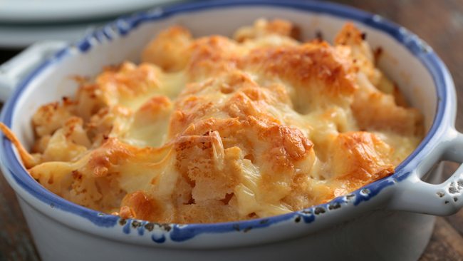 A baked dish topped with golden, melted cheese in a blue-rimmed ceramic bowl.