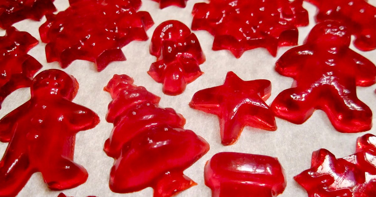 Red holiday shaped gummy candies, including stars, trees, and gingerbread figures, arranged on parchment paper.