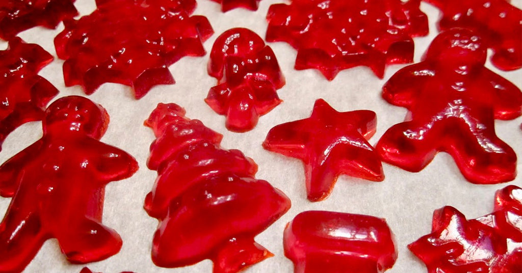 Red holiday shaped gummy candies, including stars, trees, and gingerbread figures, arranged on parchment paper.