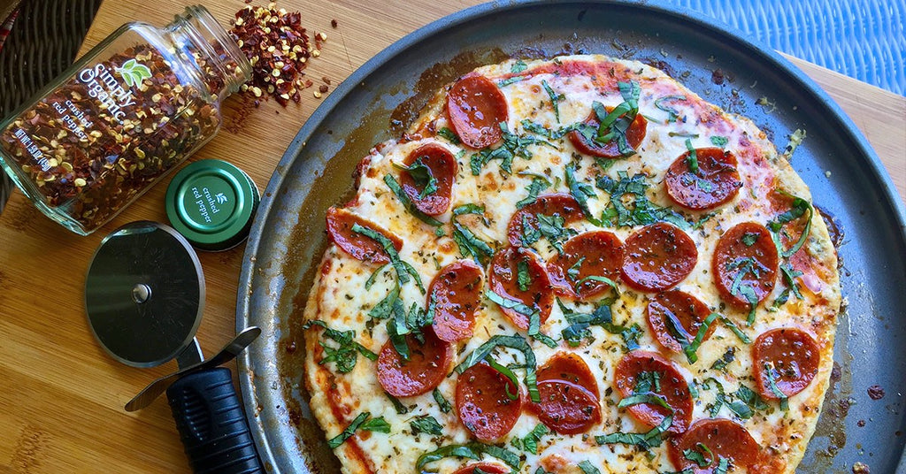 Pepperoni pizza topped with fresh basil on a pan, with crushed red pepper and a pizza cutter beside it.