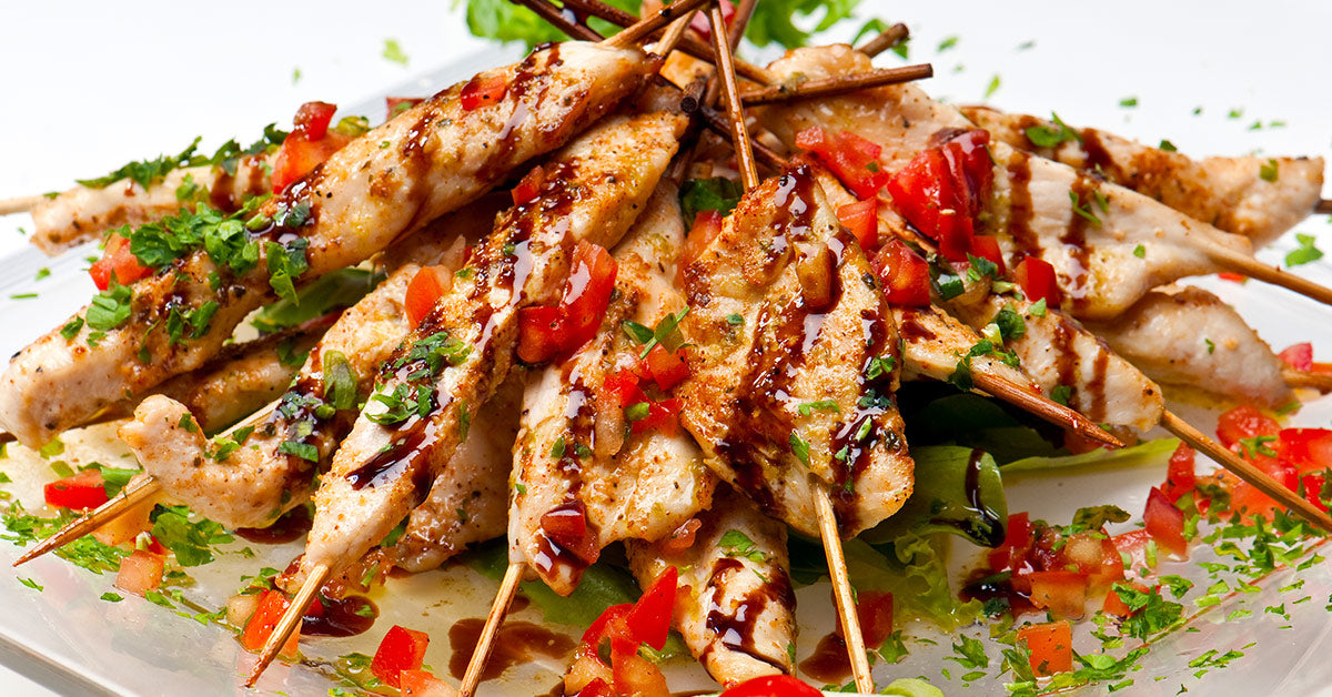 Grilled chicken skewers topped with chopped tomatoes, herbs, and a drizzle of sauce on a bed of fresh greens.