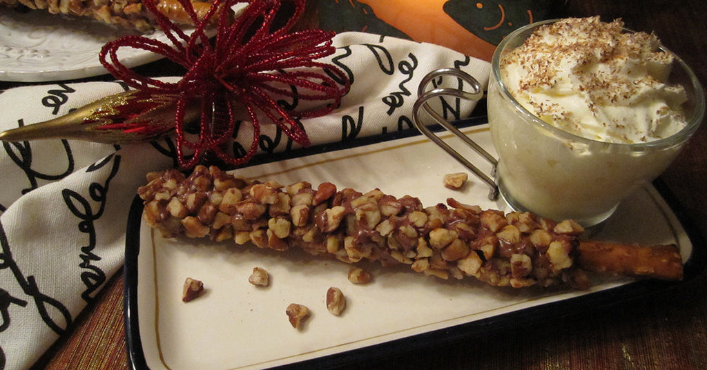 Nut-coated caramel pretzel stick served on a tray with a cup of whipped cream topped with grated chocolate.