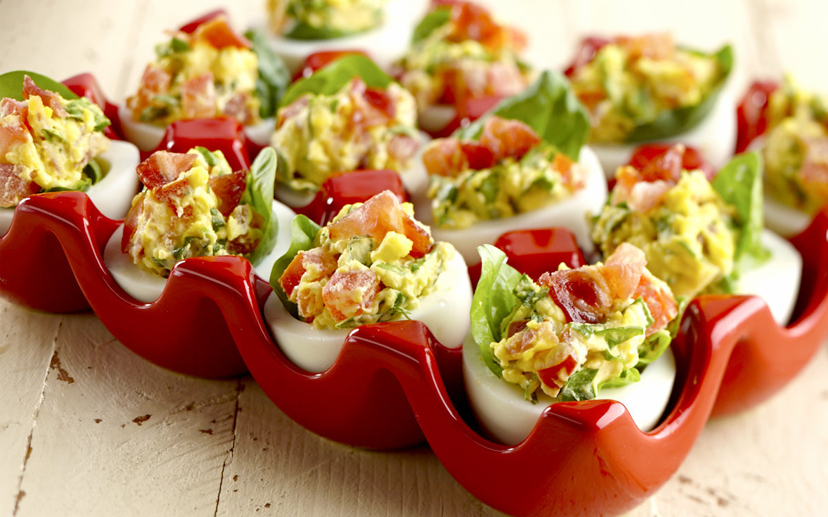 Deviled eggs filled with a colorful mix of bacon, spinach, and veggies arranged in a red ceramic egg tray.