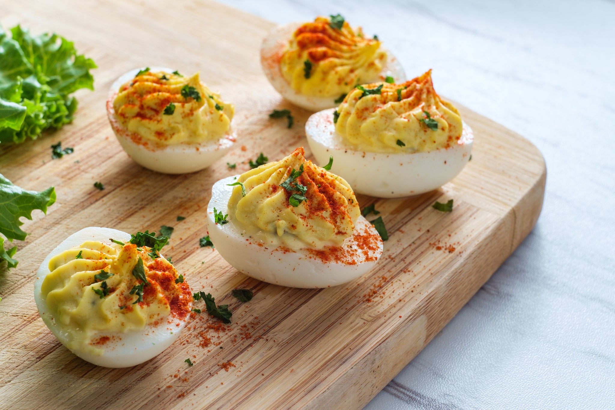 Deviled eggs topped with paprika and herbs on a wooden board.