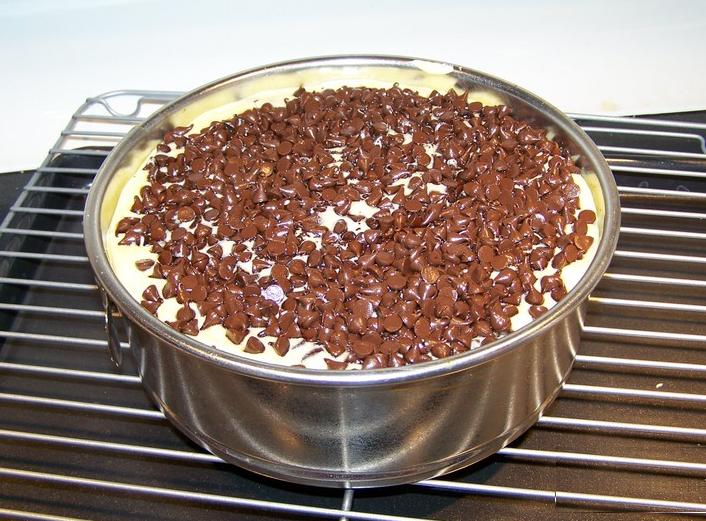 Cake pan filled with batter topped generously with chocolate chips, cooling on a wire rack.