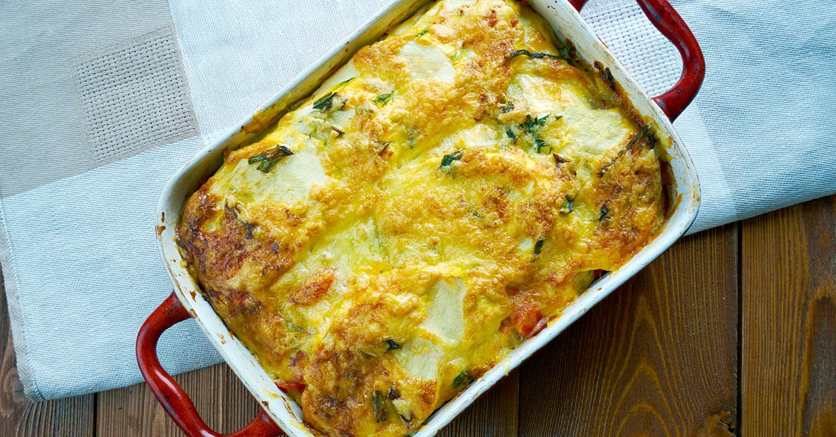 Golden baked casserole in a rectangular dish with melted cheese and herbs on top.