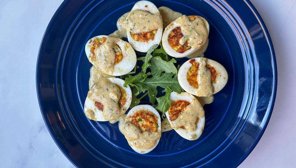 Deviled eggs arranged in a circle on a blue plate, topped with creamy sauce and garnished with arugula.