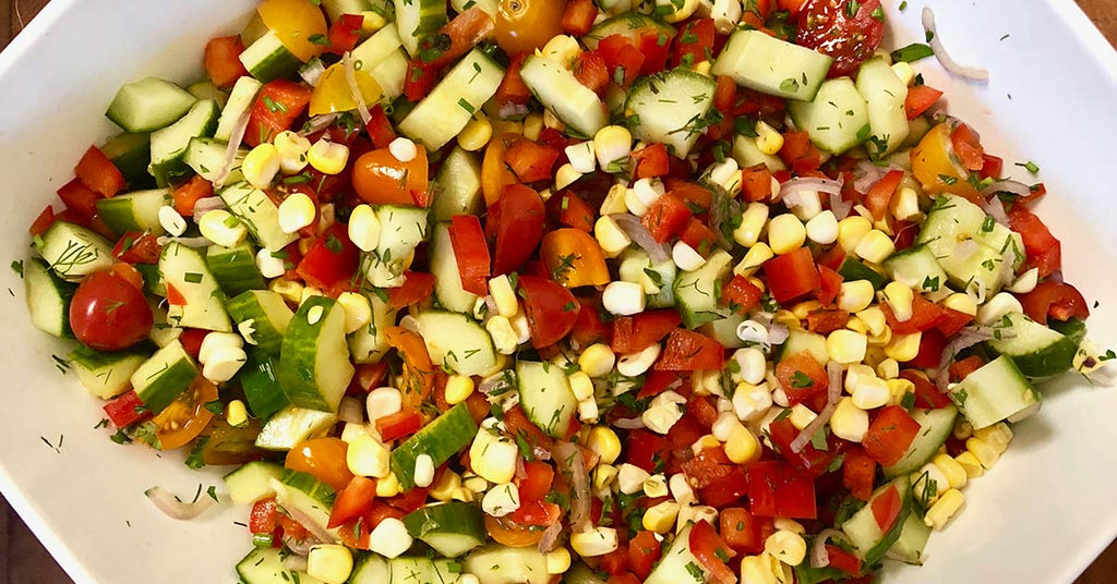 Colorful salad with cucumbers, tomatoes, corn, peppers, and herbs mixed in a white dish.