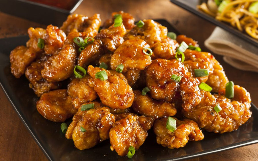 Glazed, crispy fried chicken pieces coated in a golden sauce and topped with sliced green onions on a black serving plate.