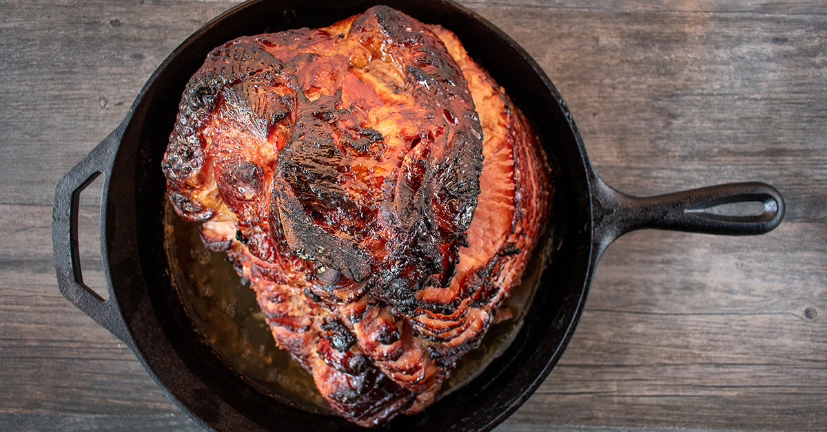 Glazed, caramelized spiral ham in a cast-iron skillet on a wooden surface.